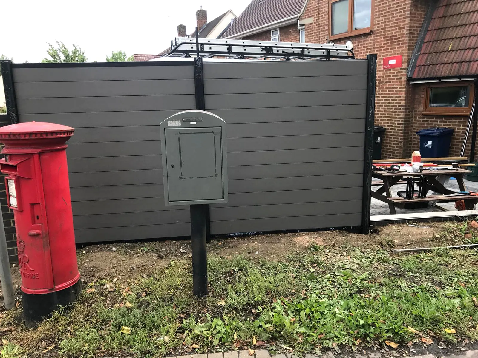 A red Royal Mail pillar box in front of new composite fencing